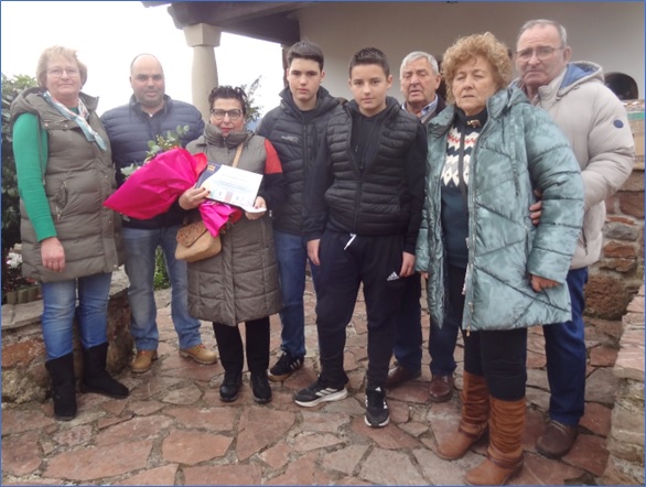 Gela (viuda del homenajeado, Julio Redondo), con un ramo de flores y mostrando la placa, junto a familiares. Por la derecha, Enrique Meana, su esposa Berta y Roberto Arboleya (presidente de la Junta Vecinal).